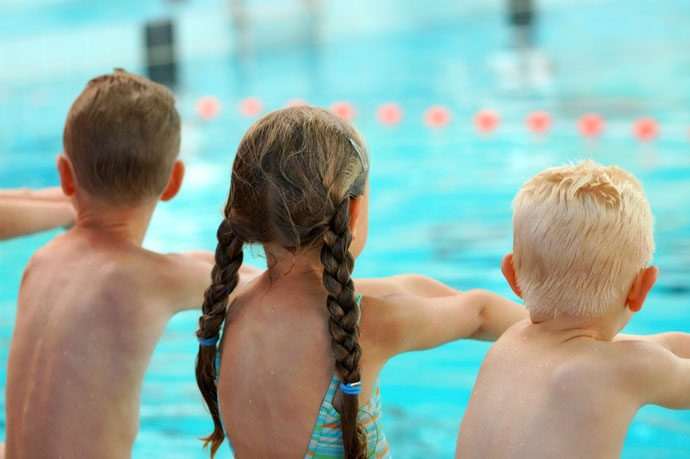 Three children practicing breaststroke movements on dry land