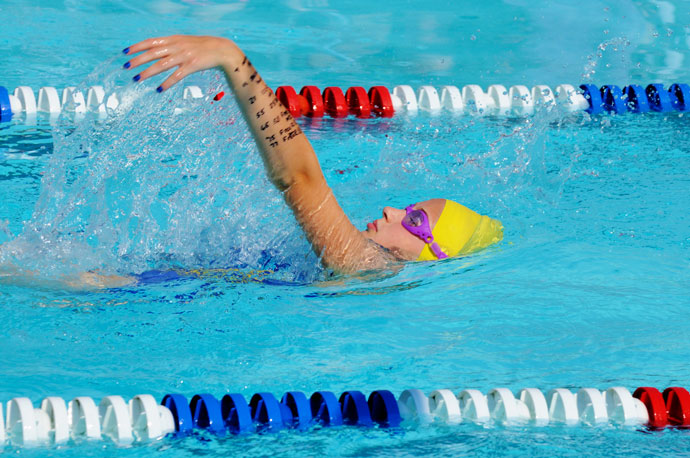 A female backstroke swimmer in an outdoor swimming pool.