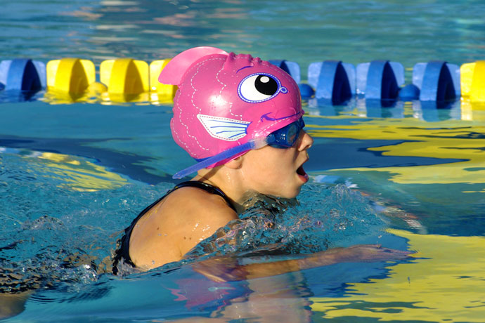Young girl with fish-like pink swim cap doing breaststroke